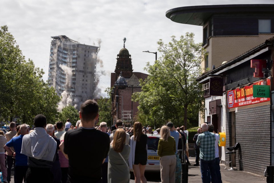 Controlled demolition of tower blocks in Glasgow, Scotland, watched by onlookers.