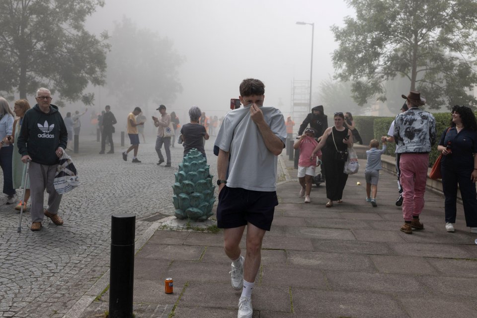 People watching demolition of tower blocks in foggy conditions.