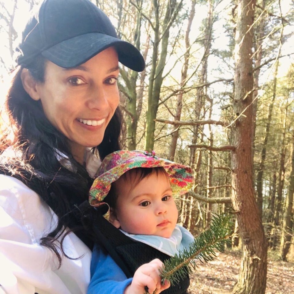 A mother and her baby in a baby carrier in a forest.