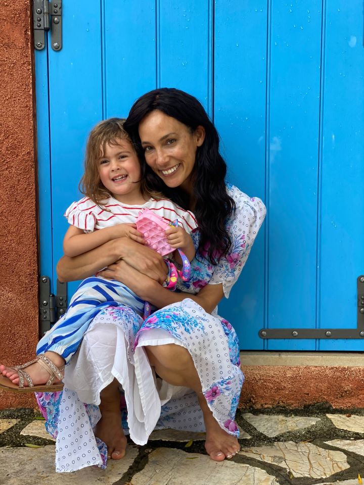 A woman and her young daughter sit together in front of a blue door.