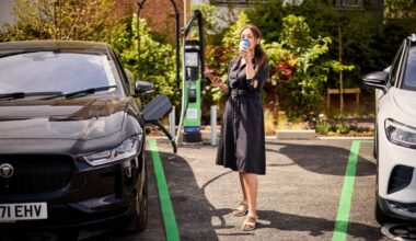 a a white woman in a black dress drinks a takeaway coffee while charging her EV
