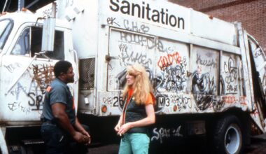a white woman stands in front of a graffitied sanitation truck talking to a black man