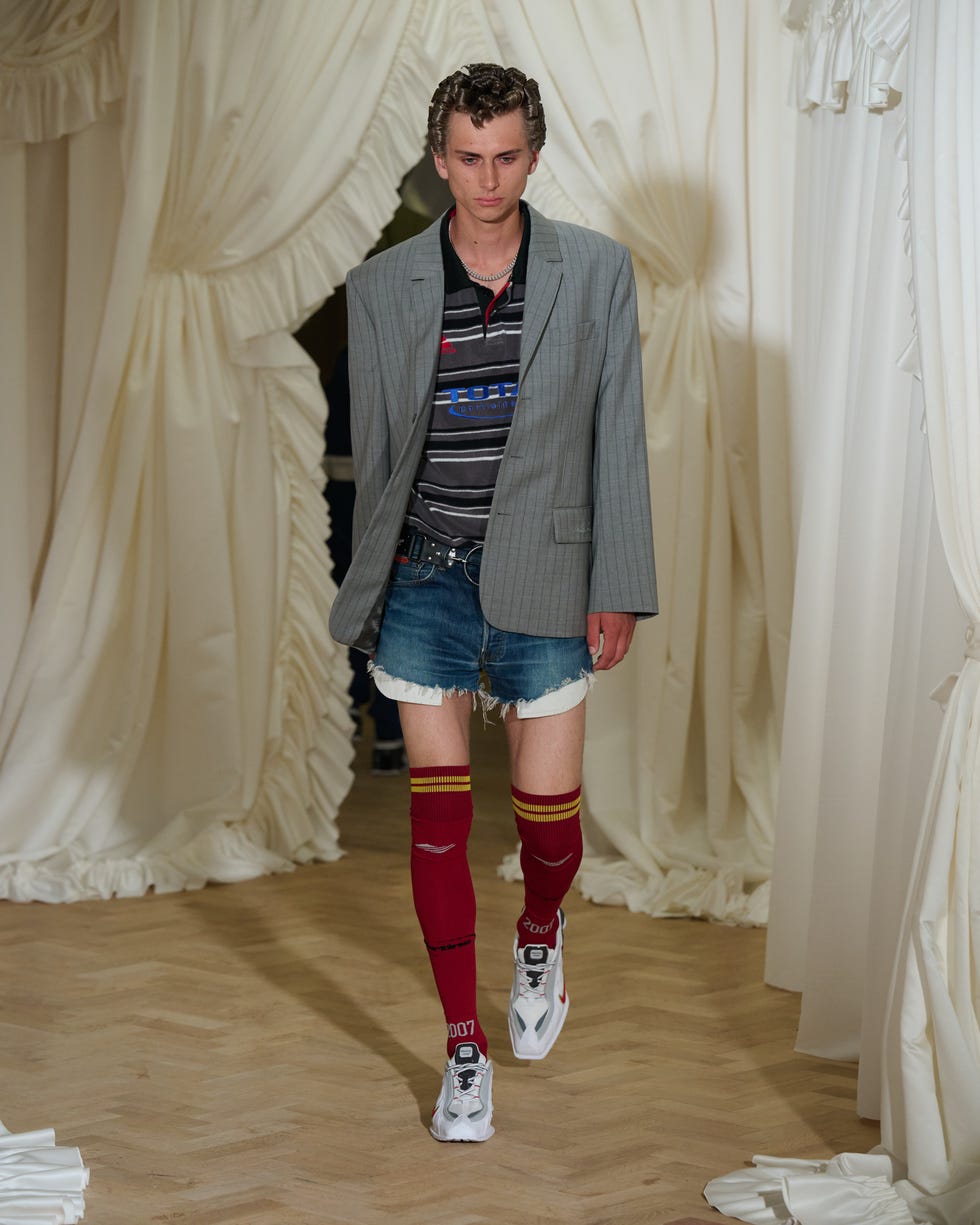 model walking on a runway wearing a unique outfit combining a blazer striped shirt denim shorts and long socks