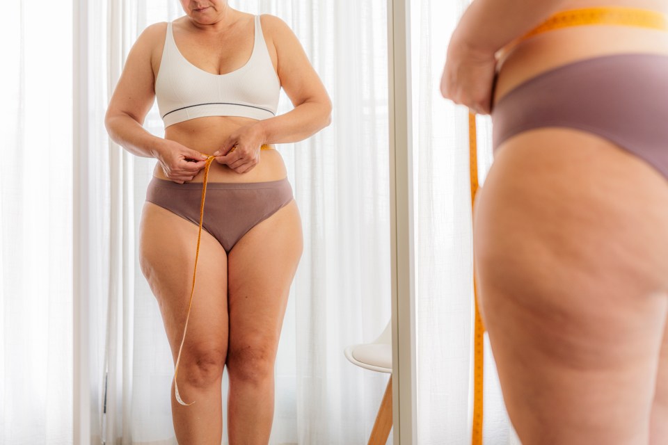 Overweight woman measuring her waist with a tape measure.
