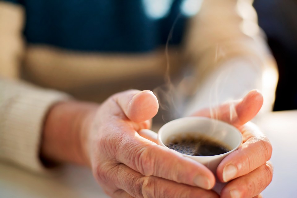 Close-up of a senior man's hands holding a steaming cup of coffee.