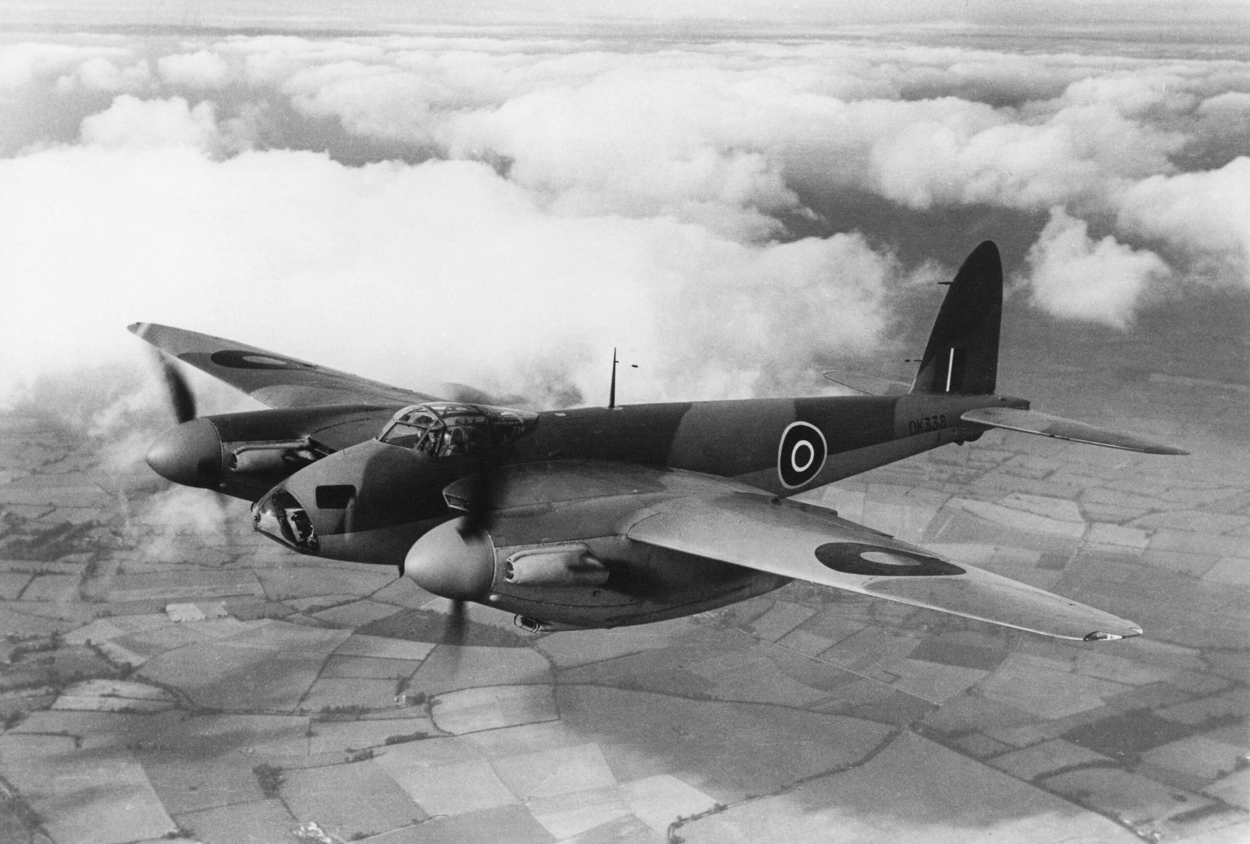 A black and white photo of a plane flying over fields.