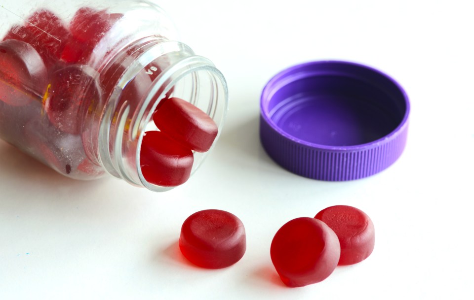Red gummy multivitamins spilling from a clear bottle with a purple lid.