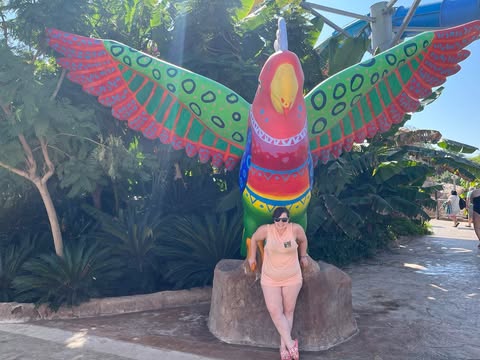Woman posing with a large colorful bird statue.