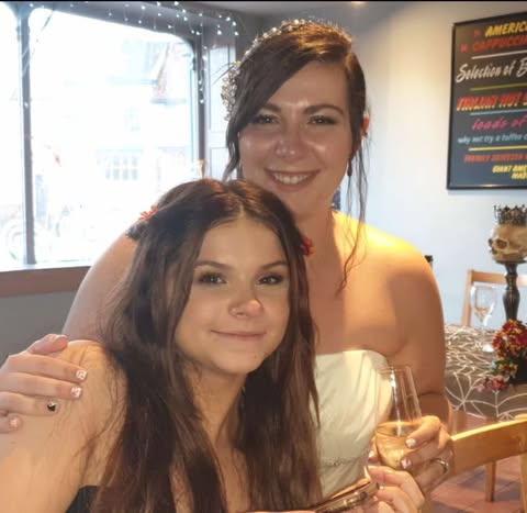Two women posing together; one is wearing a white dress.