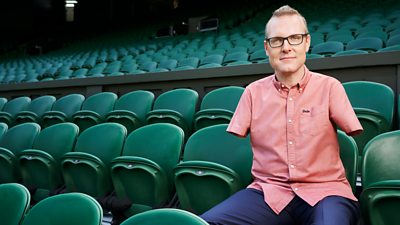 Andy Stevenson wearing a salmon pink shirt sitting on green folding chairs 
