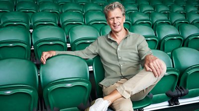 Andrew Castle wearing beige trousers and green shirt with leg crossed sitting on green folding chairs 