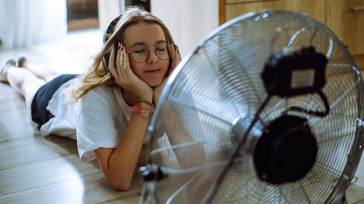 Teenage girl wearing headphones lying on the floor in front of a fan