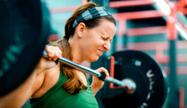 Woman holding barbell with face screwed up with effort