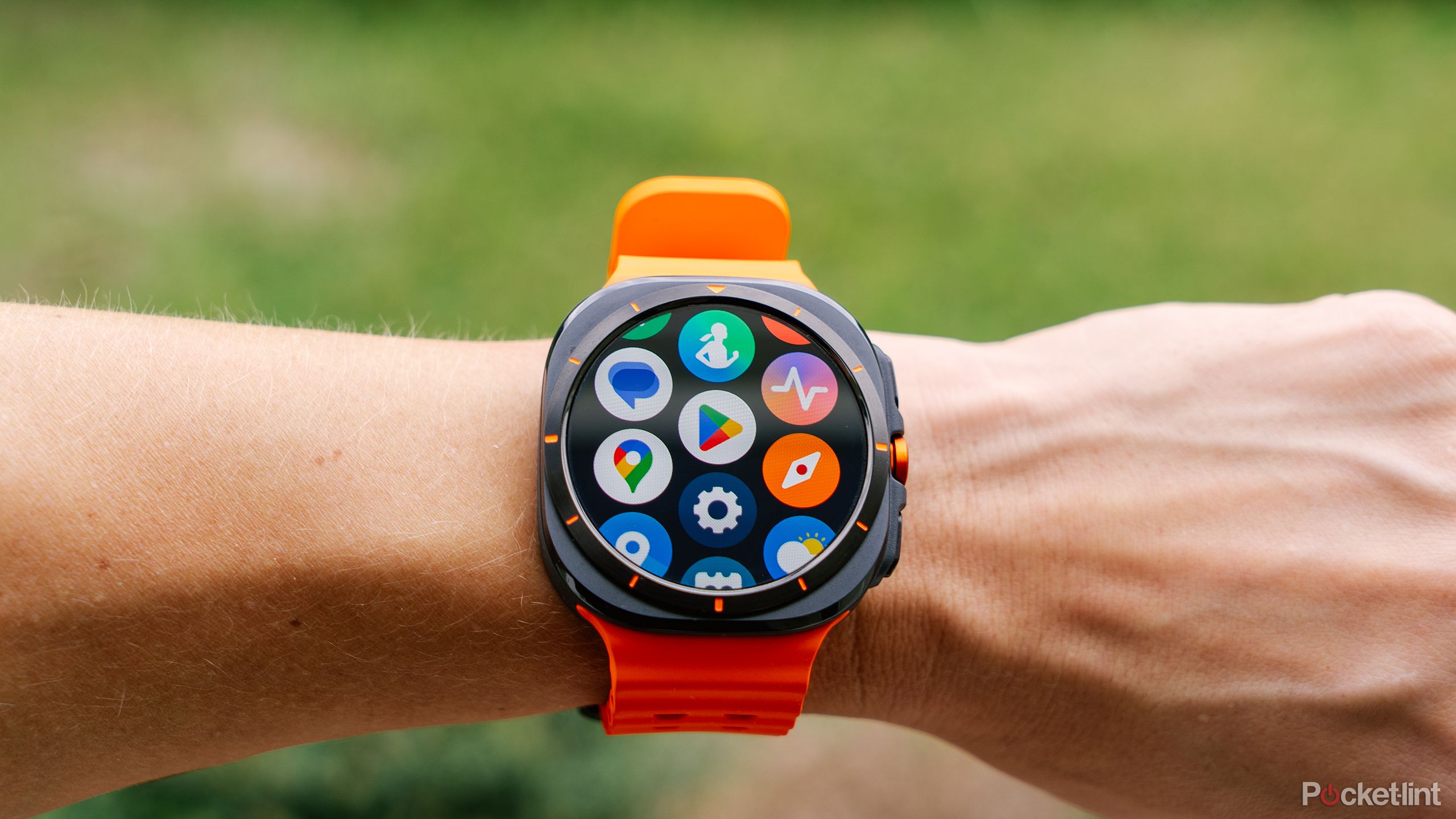A wrist with the Samsung Galaxy Watch Ultra is held in front of a blurred yard. 