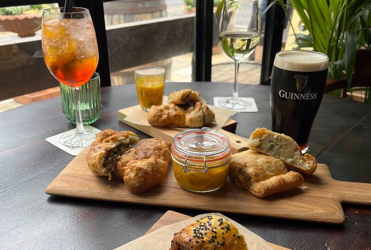 selection of pies on board with picallili and pint of Guinness, glass of wine and Aperol spritz around it on table