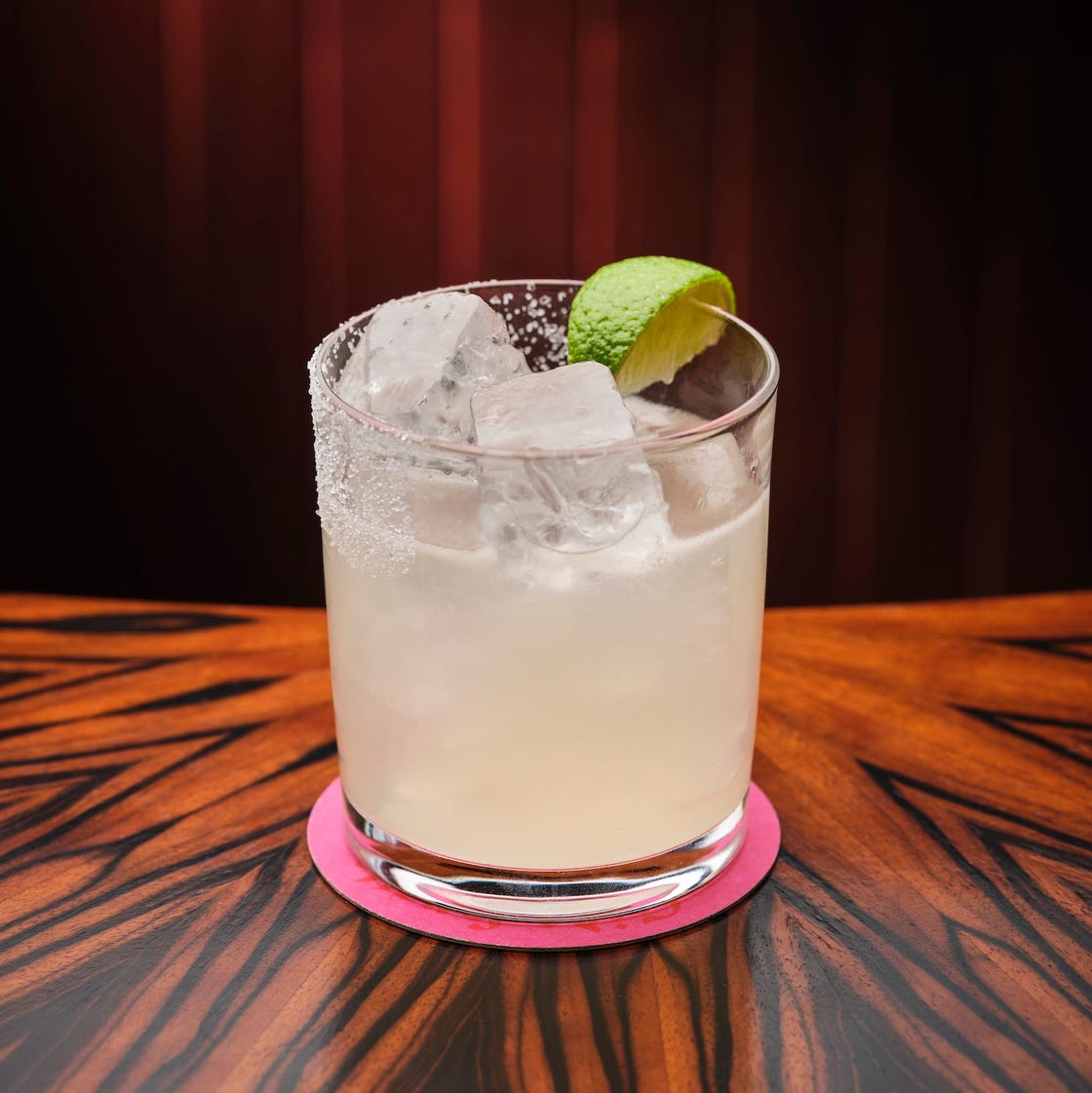 cocktail in a glass with lime garnish and ice on a wooden table