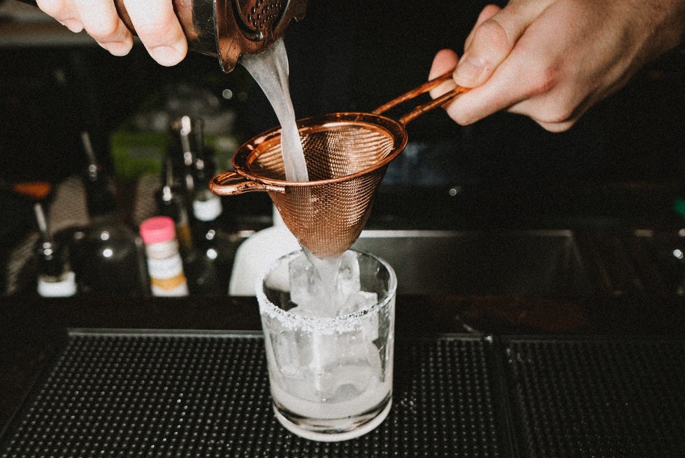 drink being poured through a strainer to make a margarita