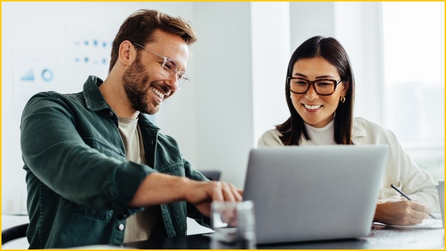 Man and woman working on a laptop computer, smiling.