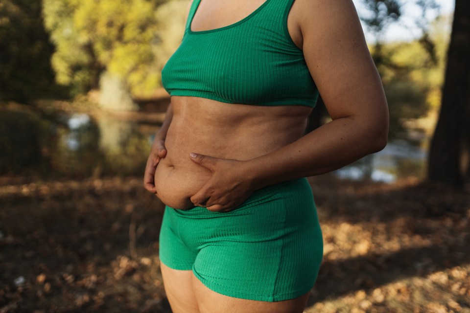 Midsection of a plus-size woman in green athletic wear standing outdoors.
