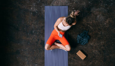 Woman seen from above sitting on yoga mat looking at smartphone with a cork yoga block next to her