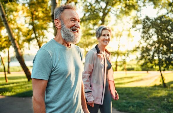 Active hobby on retirement. Grey haired caucasian man with beautiful wife strolling at summer park and smiling cheerfully. Fitness retired couple in s