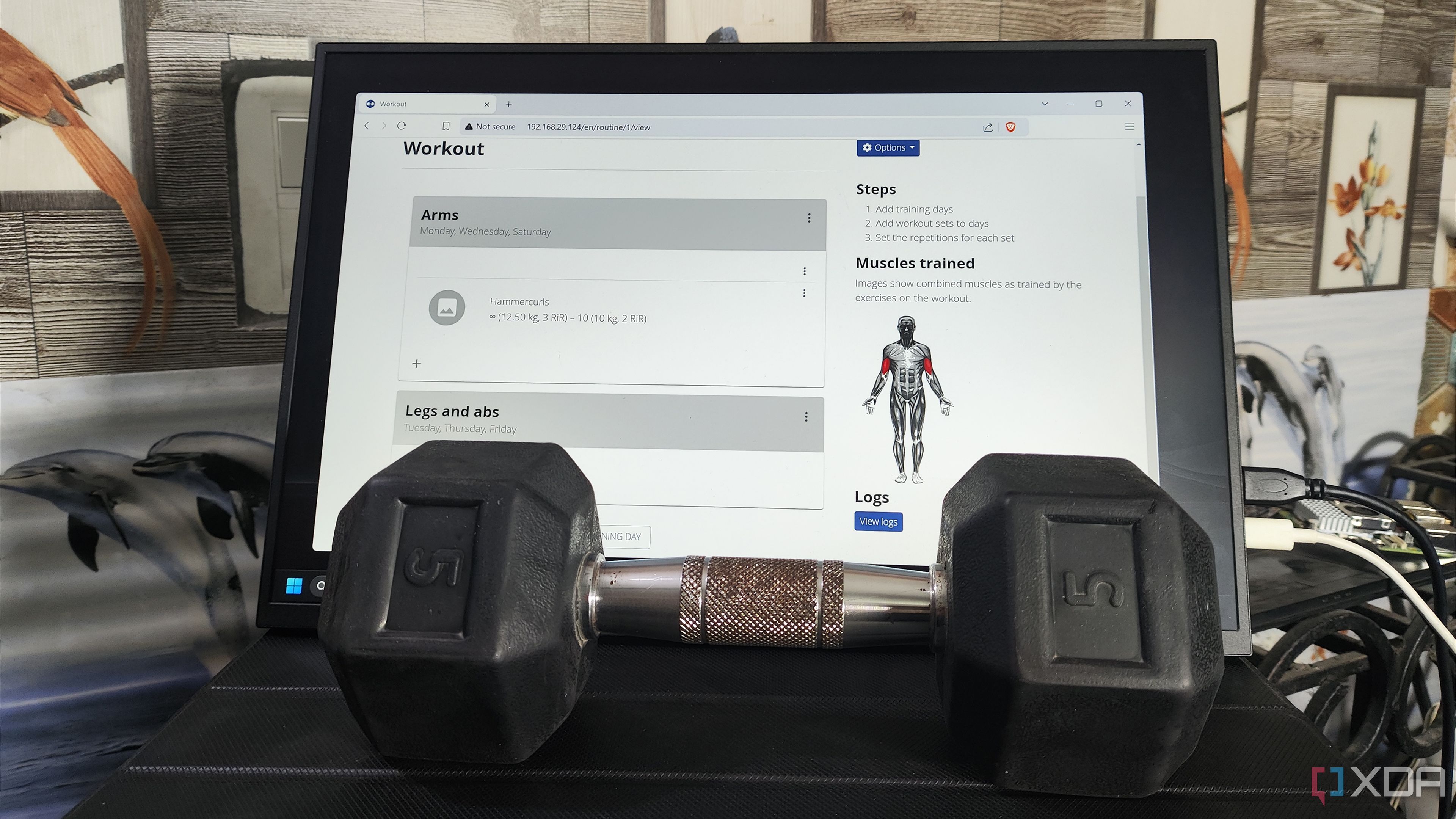 A dumbbell placed in front of a monitor displaying the wger UI