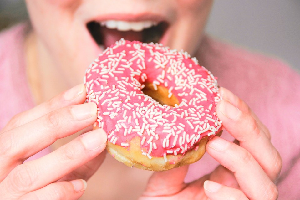 Woman taking a bite of a pink donut with white sprinkles.