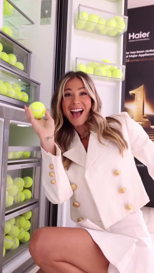 Woman in white suit holding a tennis ball in front of a refrigerator filled with tennis balls.