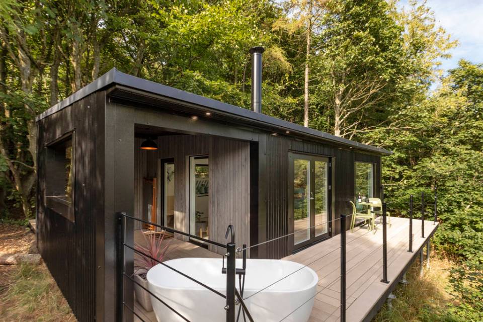 Bracken Treehouse at Airdit, Scotland: exterior view of modern treehouse with deck and freestanding bathtub.