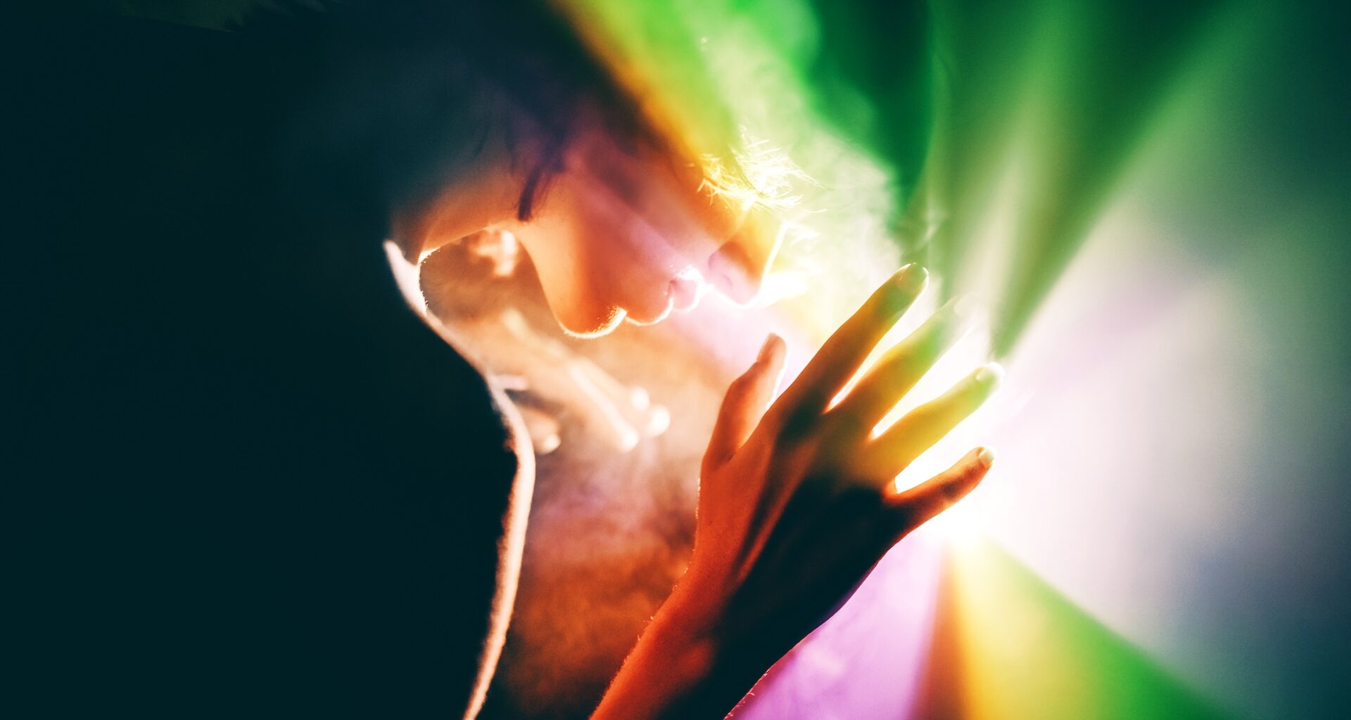 a photograph of a woman holding her hand up to a rainbow light