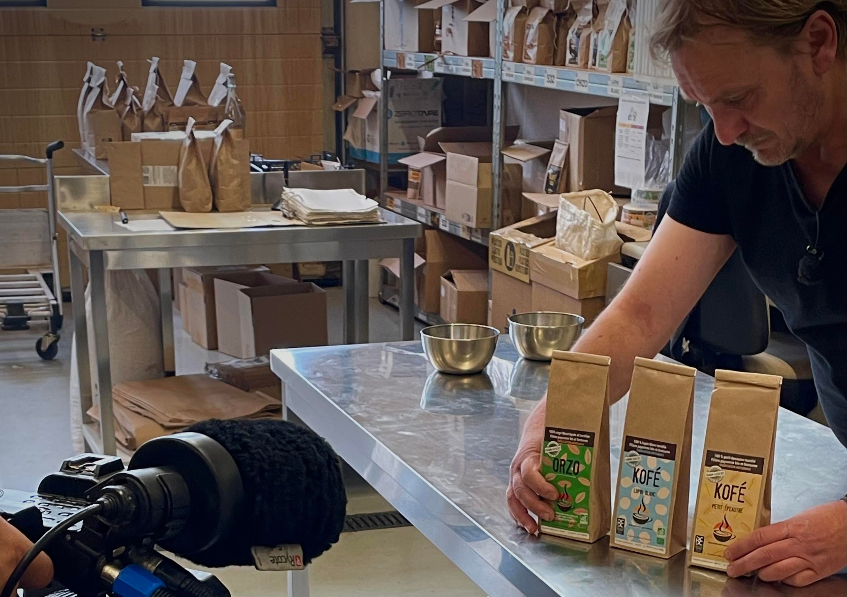Person holding bags of coffee and grain, being filmed.