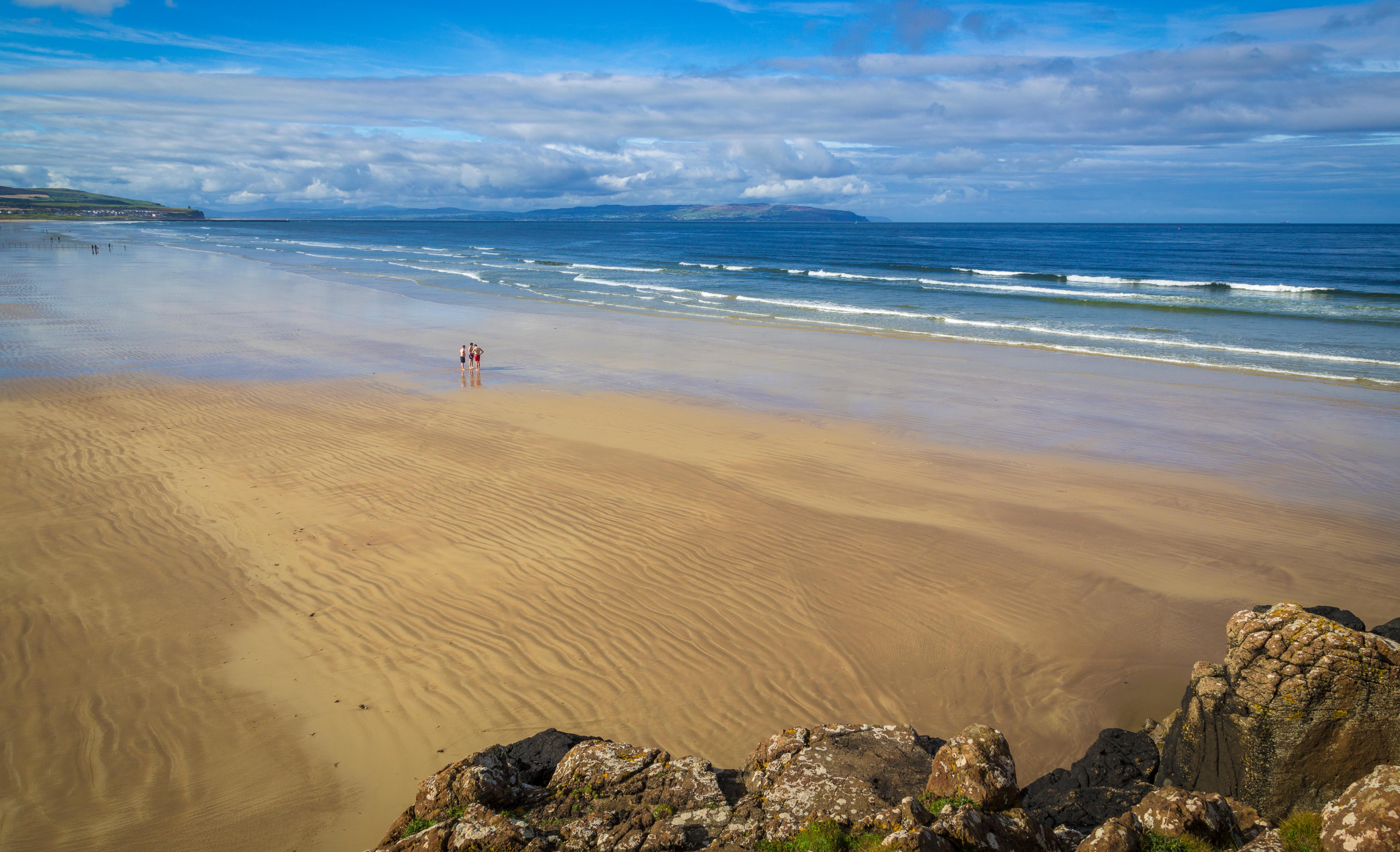 Sandy beach at Portstewart with ocean waves and people in the distance.