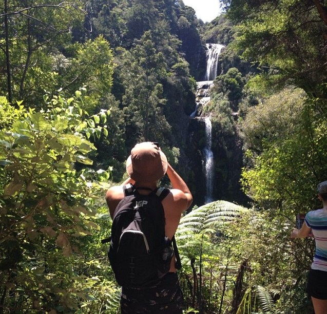 Person photographing a waterfall in a lush forest.