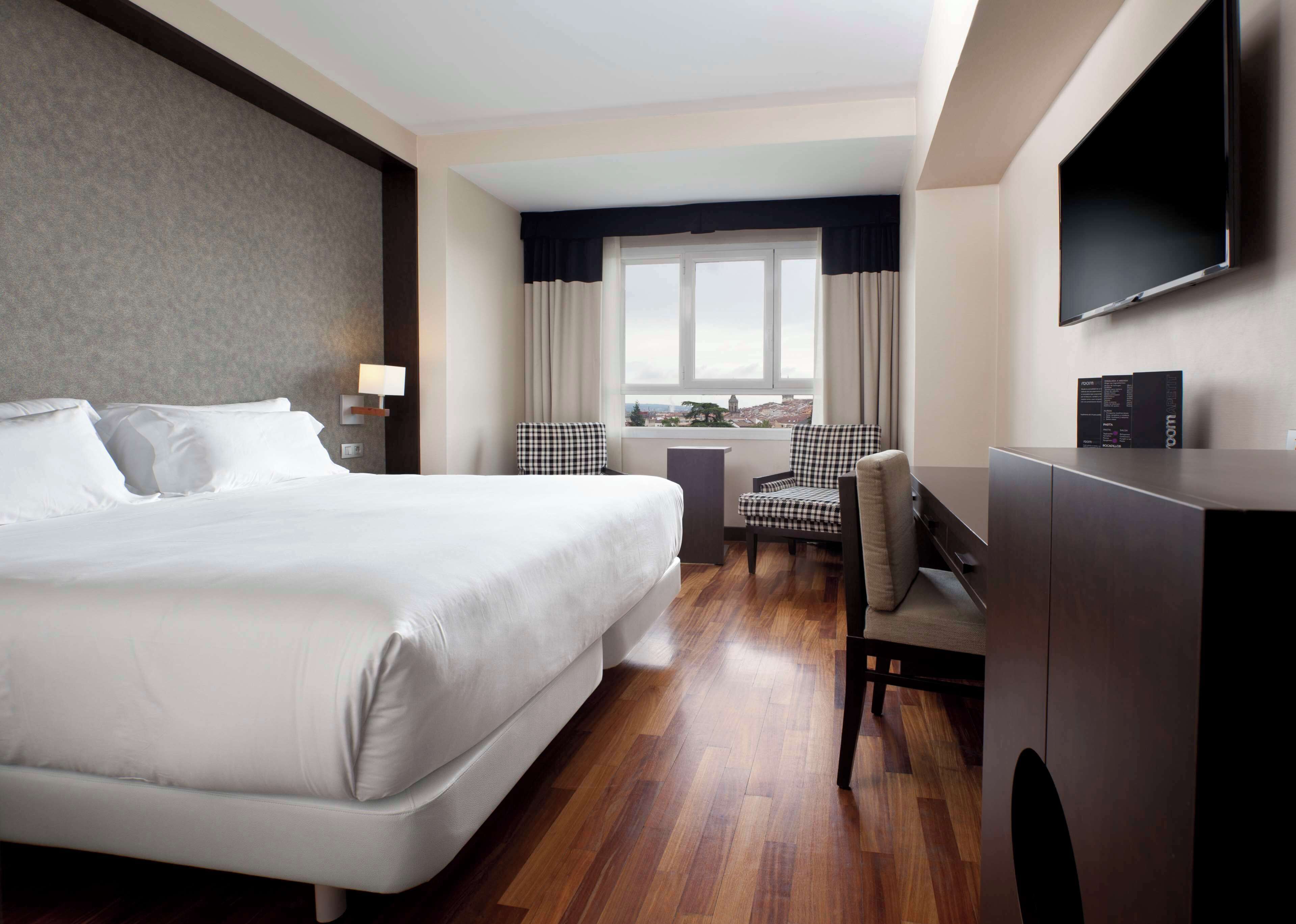 Hotel room with a large bed, desk, and city view.