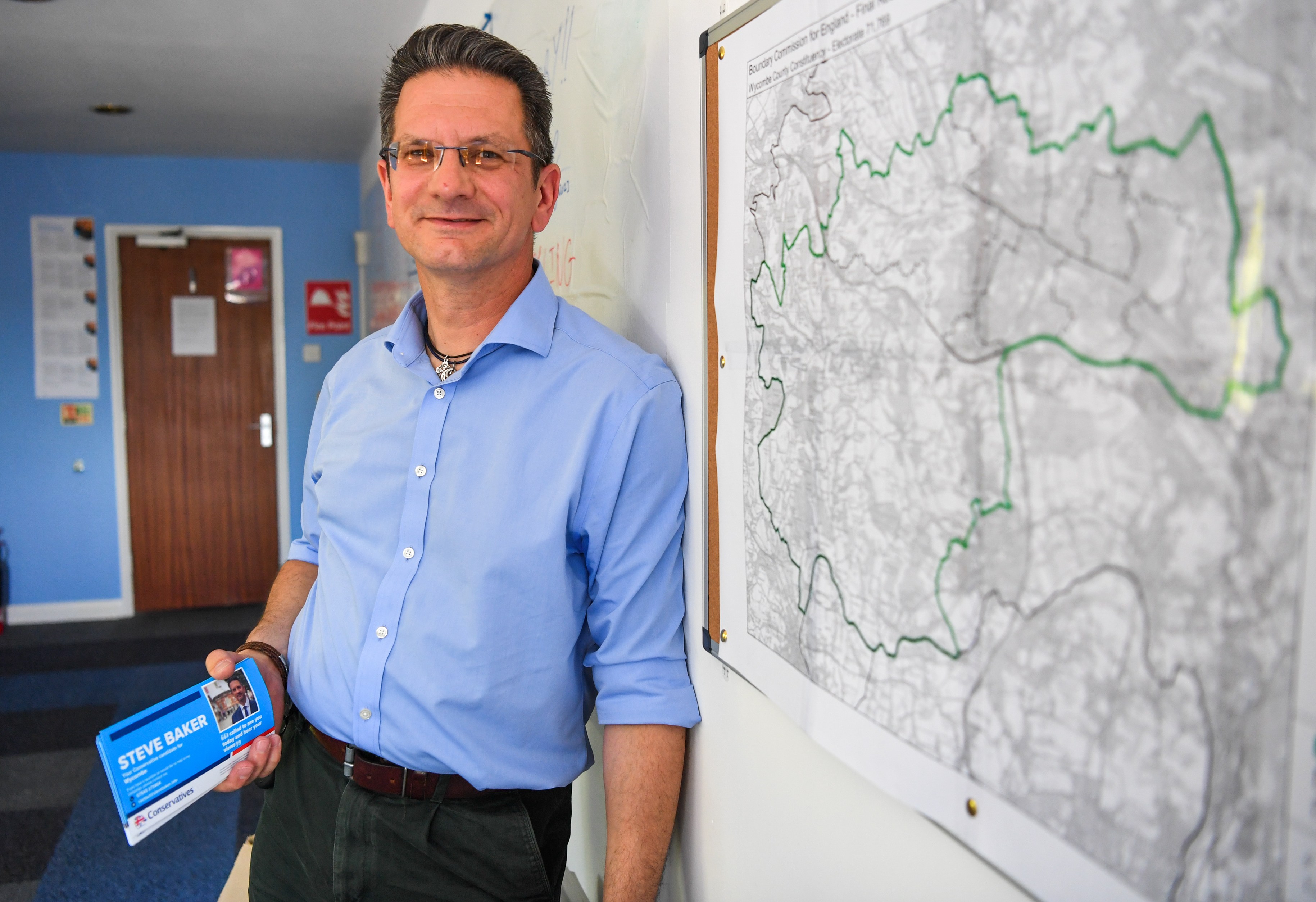 Steve Baker, Conservative MP, holding campaign leaflets, next to a constituency map.