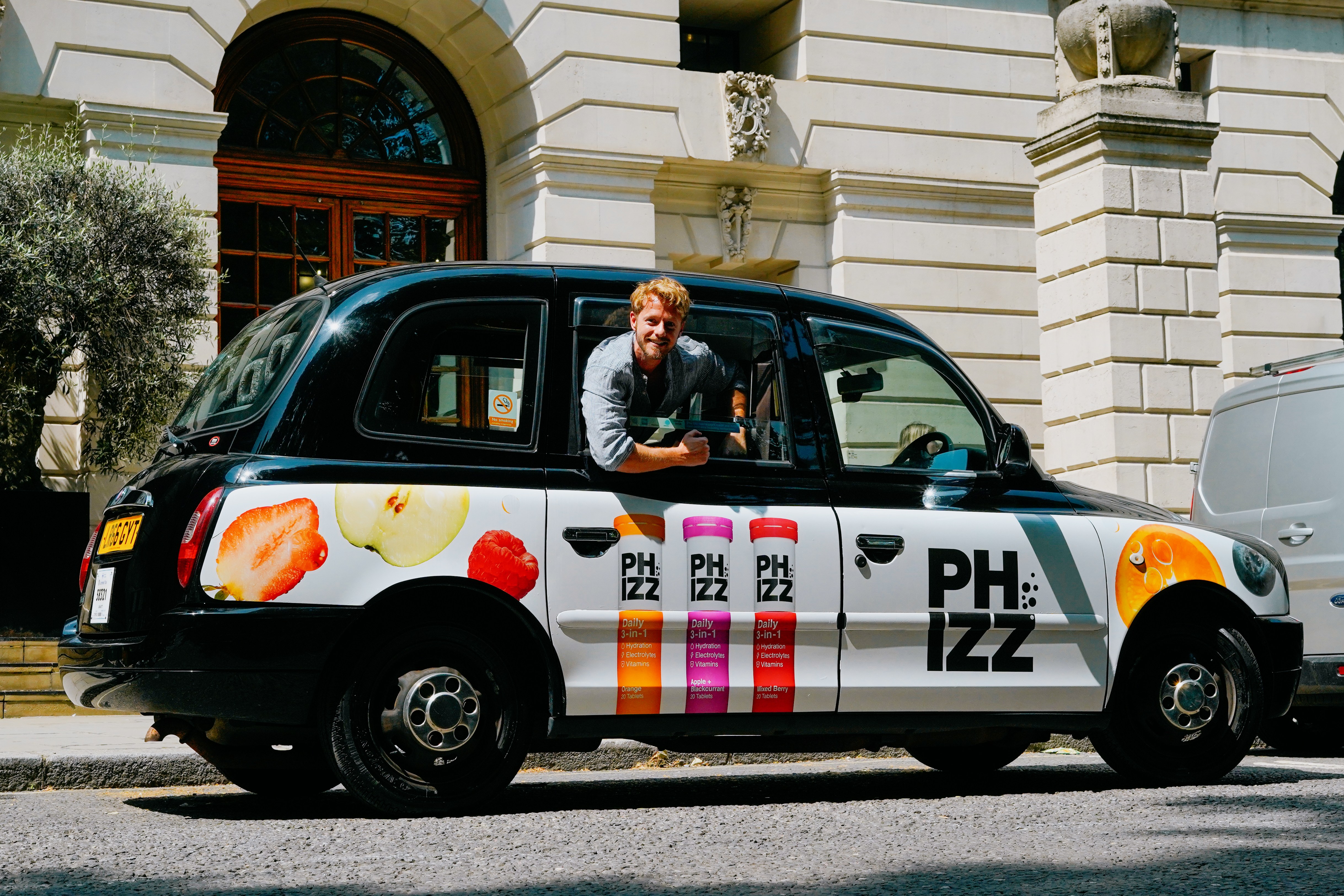 Man leaning out of a PH:IZZ branded London taxi.