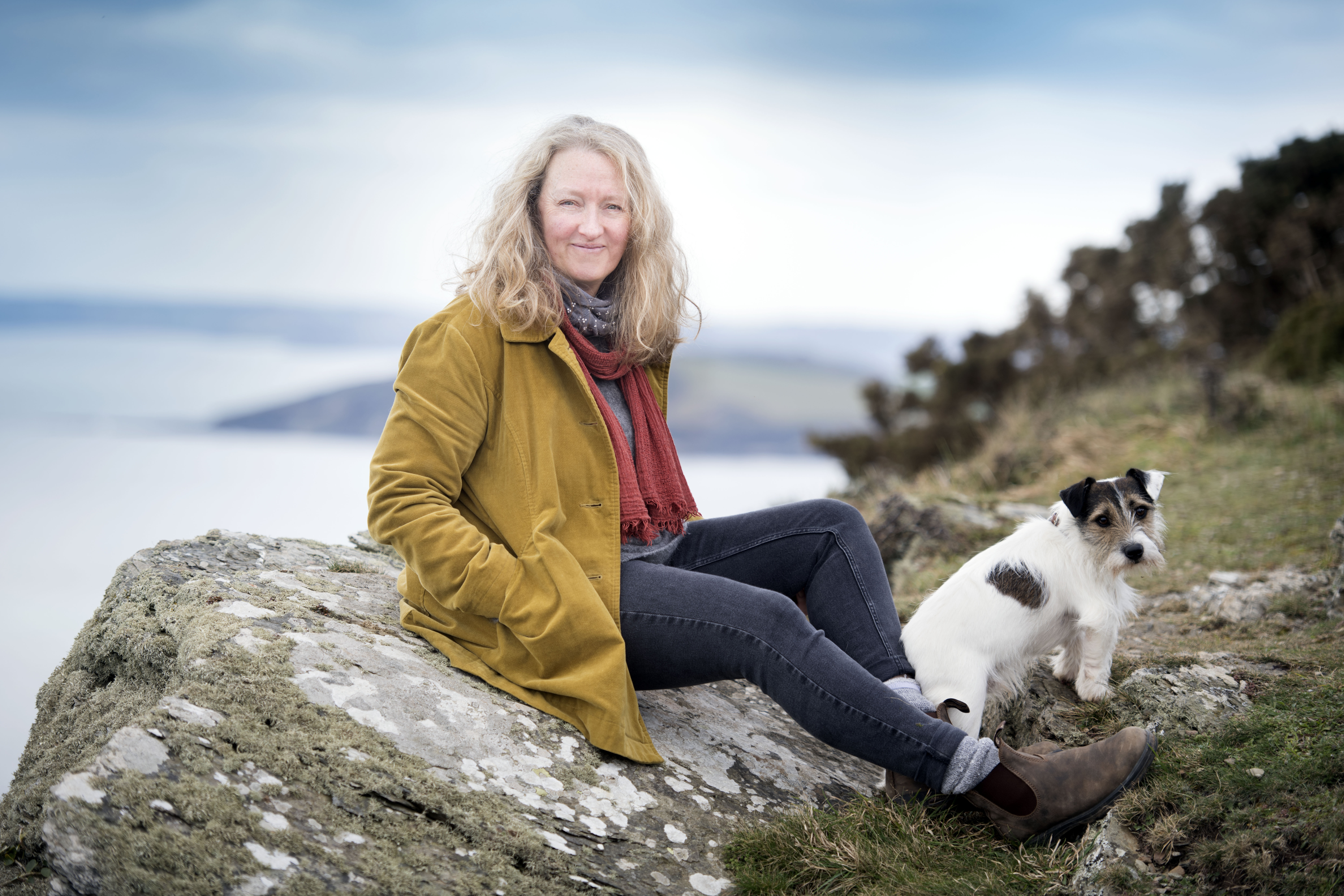Raynor Winn sitting on a rock with her dog.