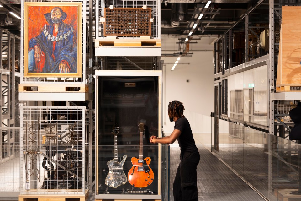 Person viewing guitars and a portrait in a museum storage facility.