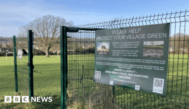 The entrance to Stoke Lodge field. there is a green gate with a large green poster reading 'please help protect your village green'.