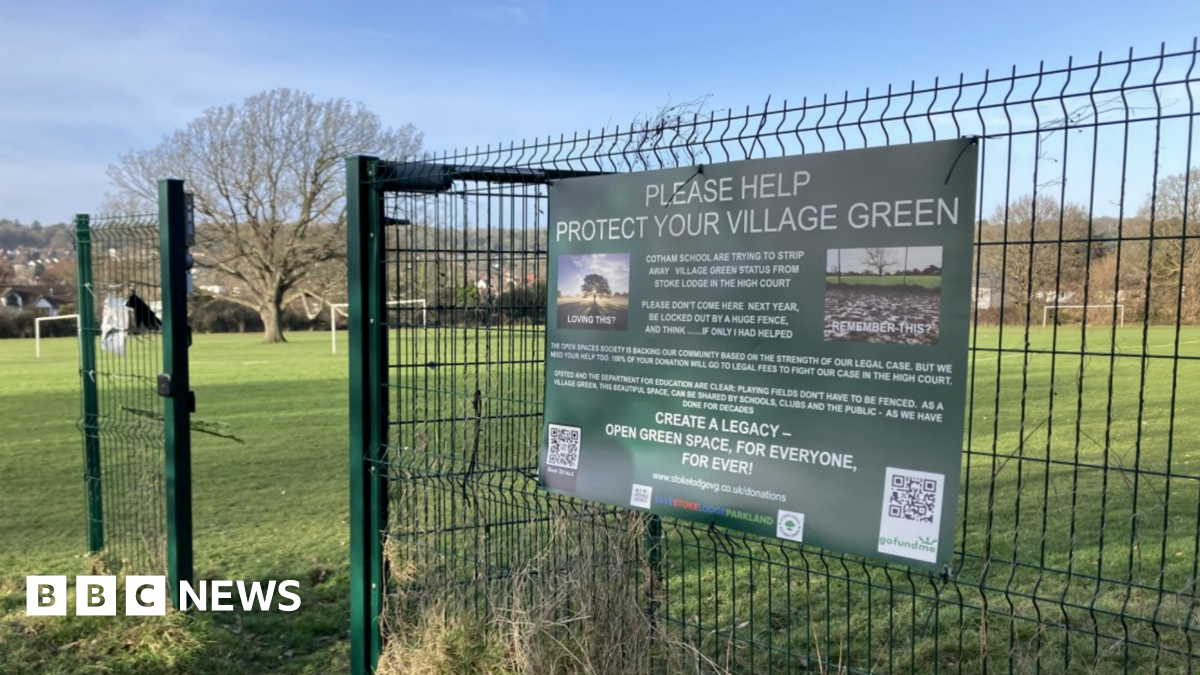 The entrance to Stoke Lodge field. there is a green gate with a large green poster reading 'please help protect your village green'.