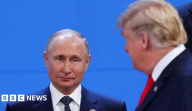 Vladimir Putin, who has thinning grey hair and wears a navy suit, white shirt and navy polka dot tie, looks toward Donald Trump, who has blonde hair combed to the side and wears a navy suit with a white shirt and red tie, at the G20 leaders summit in 2018
