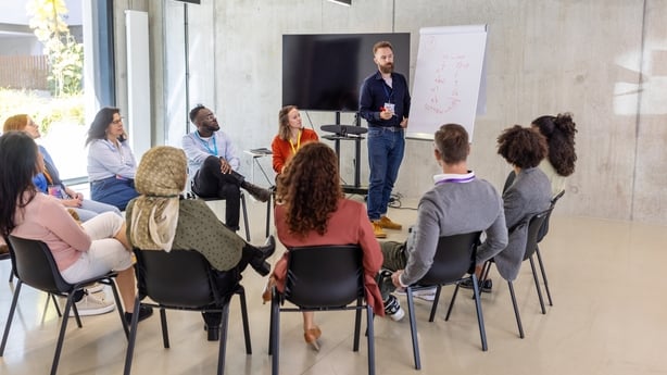 Businessman engaging a diverse group of professionals by presenting concepts on a flipchart. Showcases teamwork and interactive learning during a conference session in a formal setting.