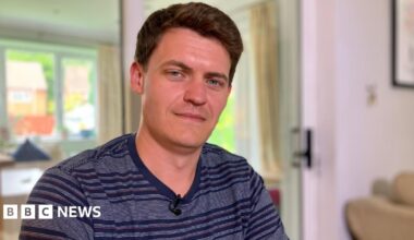 Dave in his home wearing a blue striped t-shirt, with short black hair, smiling at the camera.