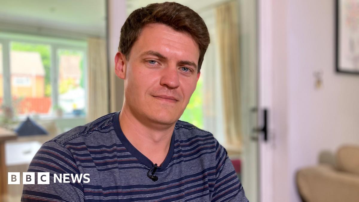 Dave in his home wearing a blue striped t-shirt, with short black hair, smiling at the camera.