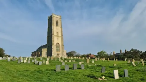 Chris Morgan/Geograph A 15th Century church surrounded by its graveyard. There are many gravestones, and there are some houses next to one of its boundaries. 