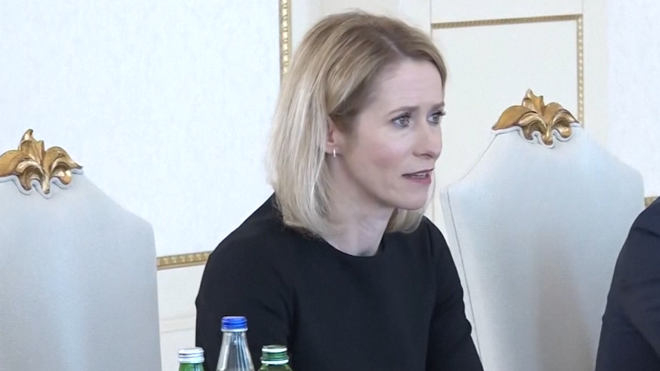 A woman with blonde hair and a black top sits on a white chair with a gold-leaf decoration
