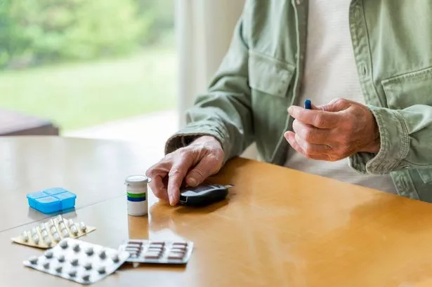 A selection of medications on a table while someone tests blood sugar levels