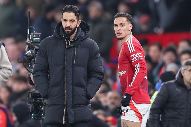Antony stands next to Ruben Amorim on the Old Trafford touchline.