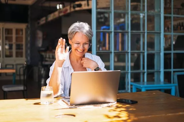 Middle aged woman with grey hair in casual clothes working at laptop in cafe