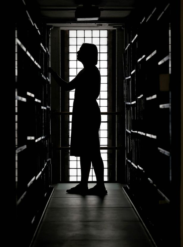 A woman silhouetted against a window peruses the shelves at the John Rylands library